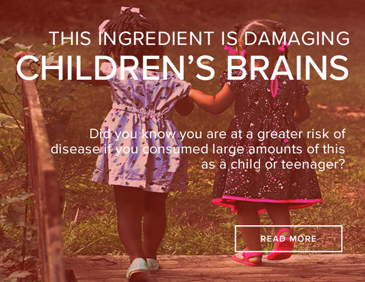 Little black girl wearing a blue spotted dress and a little white girl wearing a black dress with pink dots are holding hands as they cross a bridge to a grassy field. The image reads, "The ingredient is damaging children's brains."