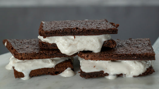 Three sugar-free ice cream sandwiches are stacked pyramid style. The cookie is dark brown and the white ice cream artfully spills out of the cookies it is sandwiched between.