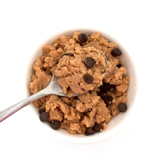 A spoonful of sugar free chocolate chip cookie dough is held above a white bowl filled with sugar free chocolate chip cookie dough. The recipe is from VegAnnie. VegAnnie and Lakanto work to provide healthy sugar-free recipes to everyone.